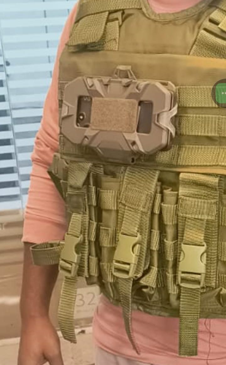 Low-profile tan node mounted on a chest harness panel, close up