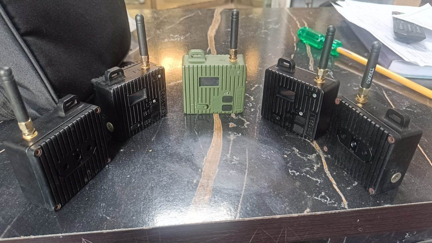 Rugged cased Meshtastic nodes in black and olive drab, each with a whip antenna and front status display
